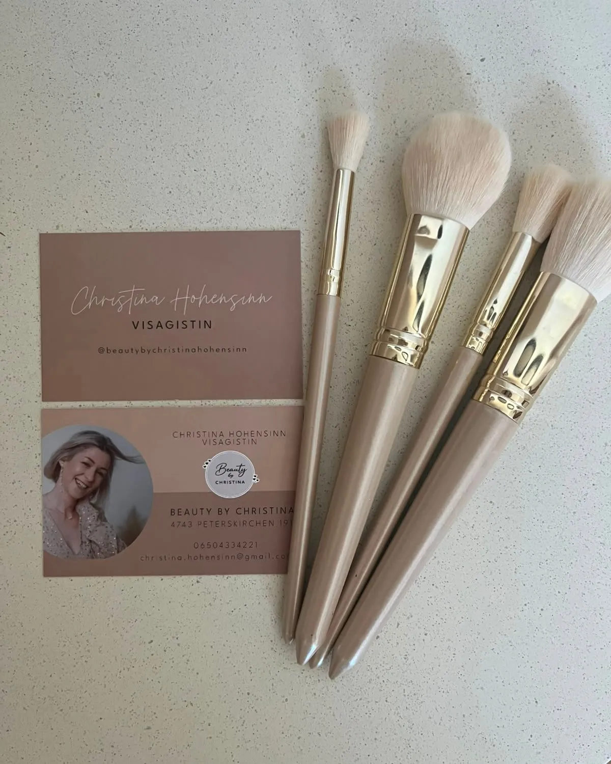 Vier cremefarbene Make-up-Pinsel neben den Visitenkarten von Beauty by Christina