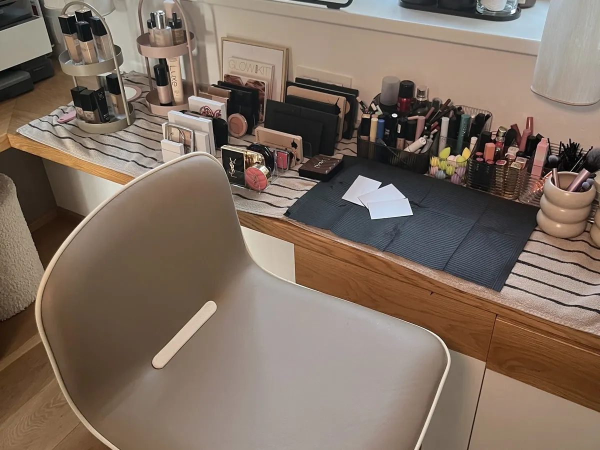 Heller Styling-Stuhl vor dem Schminktisch mit sortierter Kosmetik im Studio von Beauty by Christina
